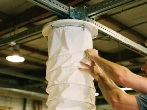 Persoon installeert witte textiele luchtkanaal aan plafondmontage in industriële werkplaats met zichtbare balken
