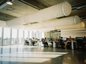 Moderne kantoorruimte met witte textiele luchtkanalen aan het plafond die frisse lucht verspreiden boven werkende medewerkers