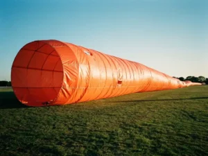 Grote oranje luchtzak windindicator wappert dramatisch in open veld tegen heldere blauwe hemel tijdens gouden uur